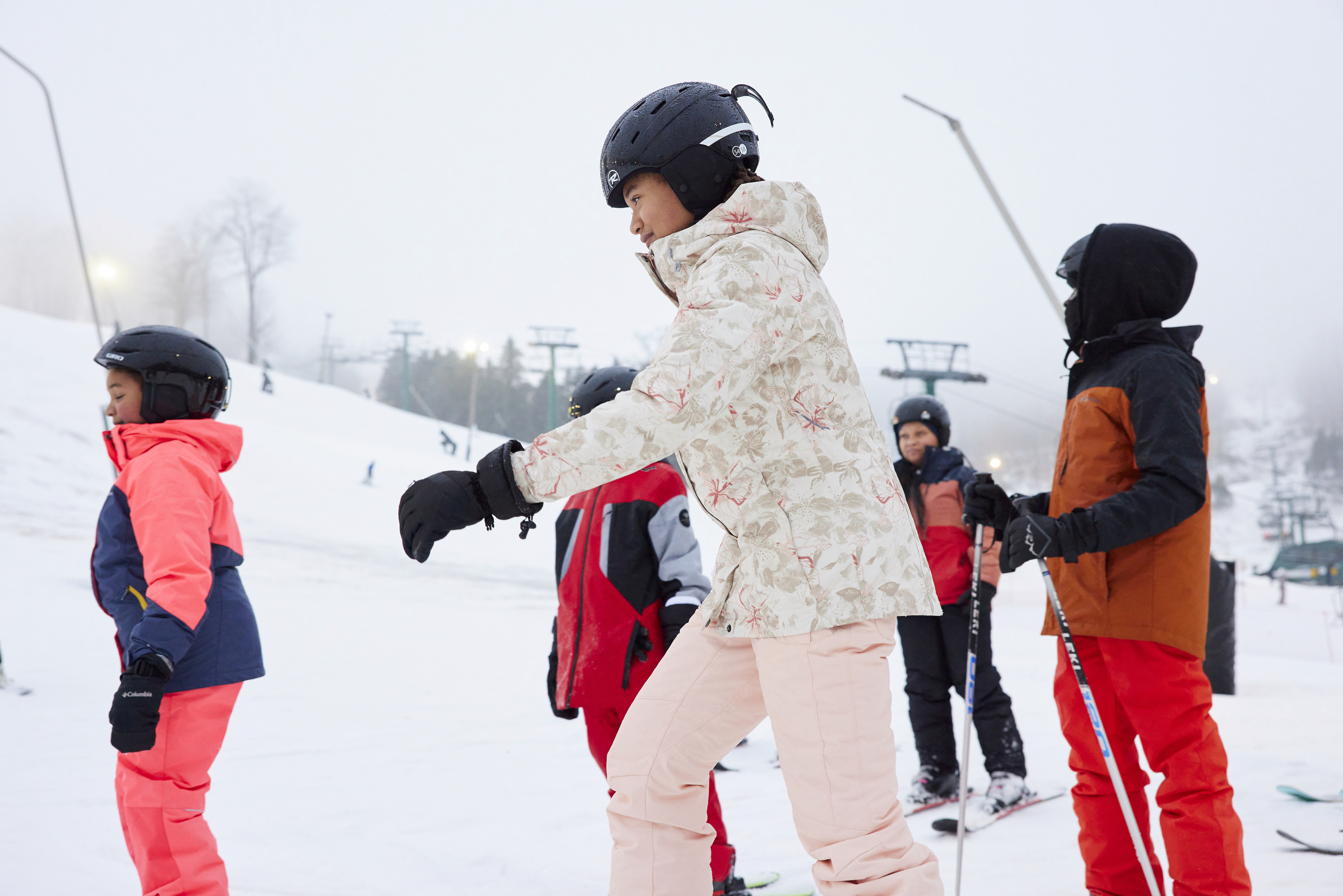 A group of young people stand in the snow ready to ski and snowboard